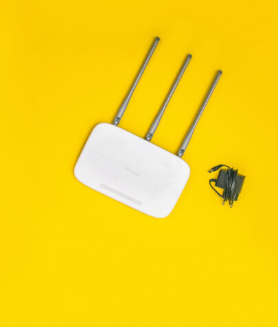 A white Wi-Fi router with three antennas placed on a yellow backdrop