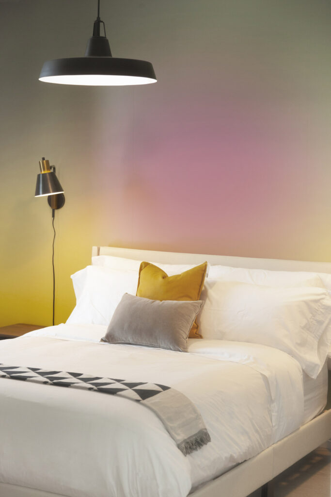 Queen sized bed with white bed linens against a yellow and pin sunburst wall paper